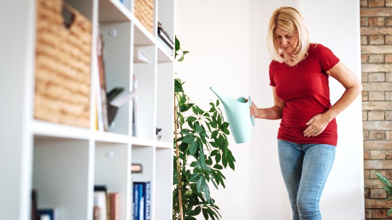 Blonde Frau in rotem T-Shirt hält sich die Hand an den Bauch wegen Unterleibsschmerzen