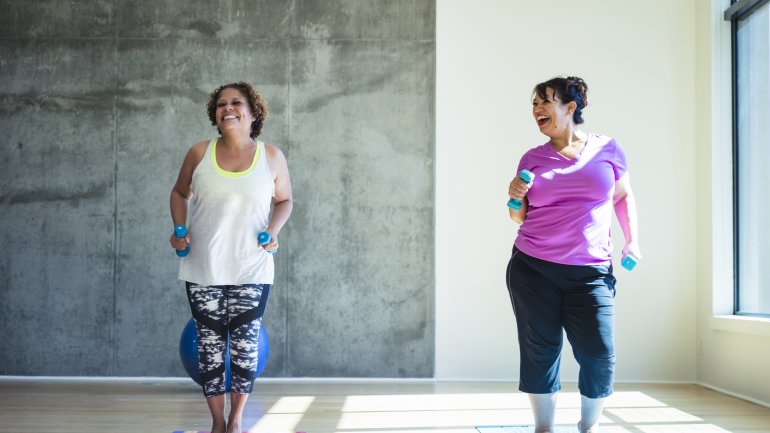 Zwei mehrgewichtige Frauen in den Wechseljahren machen zusammen Sport mit Hanteln im Fitnessstudio
