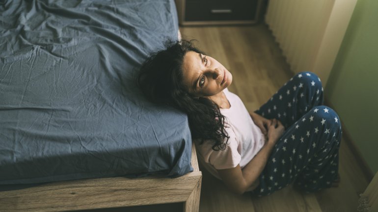 Frau mit Schlafstörungen in den Wechseljahren sitzt vor dem Bett.